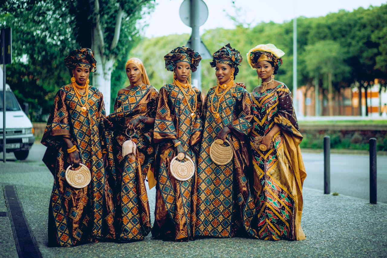 Group of African women in vibrant traditional clothing posing outdoors, showcasing cultural fashion.