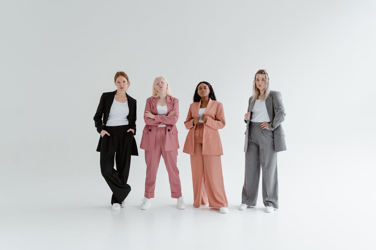 Four diverse women confidently posing in stylish suits against a plain white background.